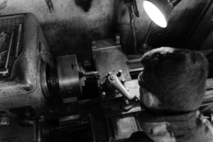 Black and white photo of a man operating an industrial lathe in a workshop.